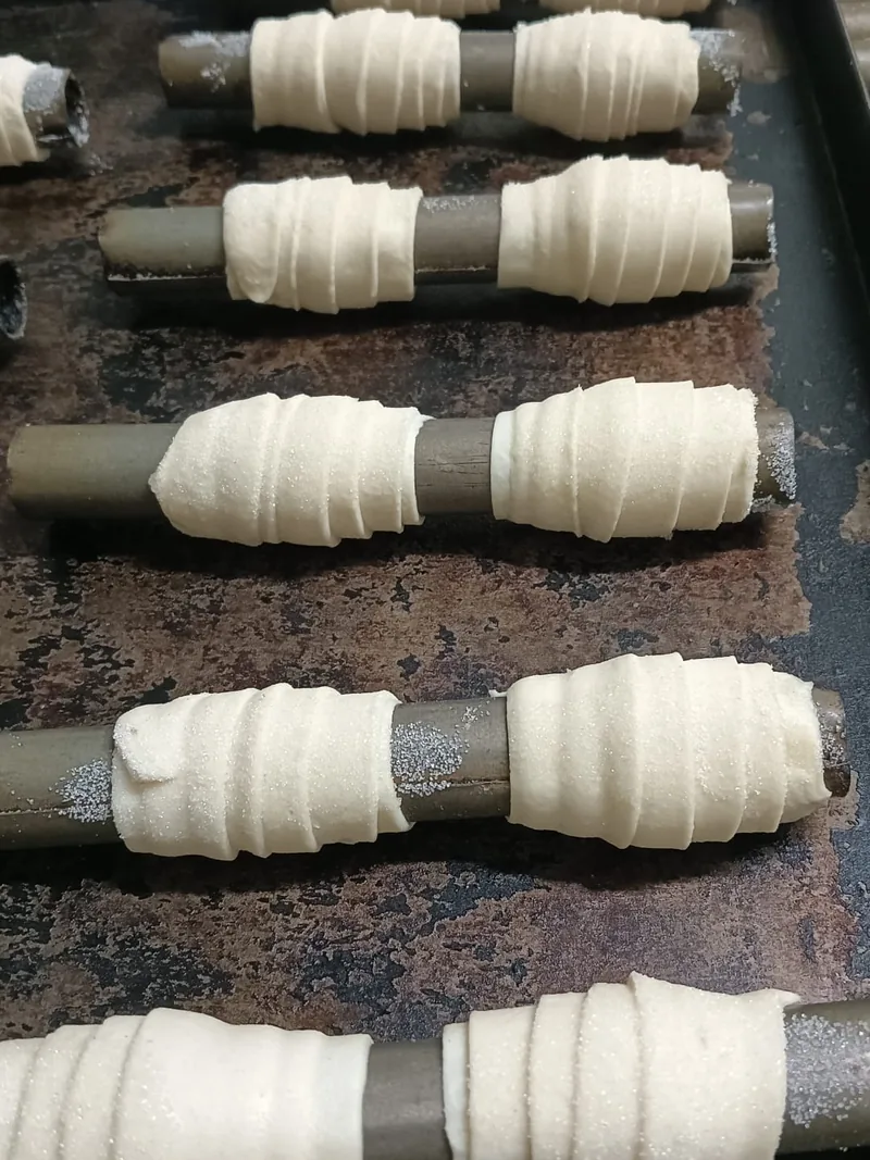 Cannoncini di sfoglia crudi arrotolati sui tubi di metallo