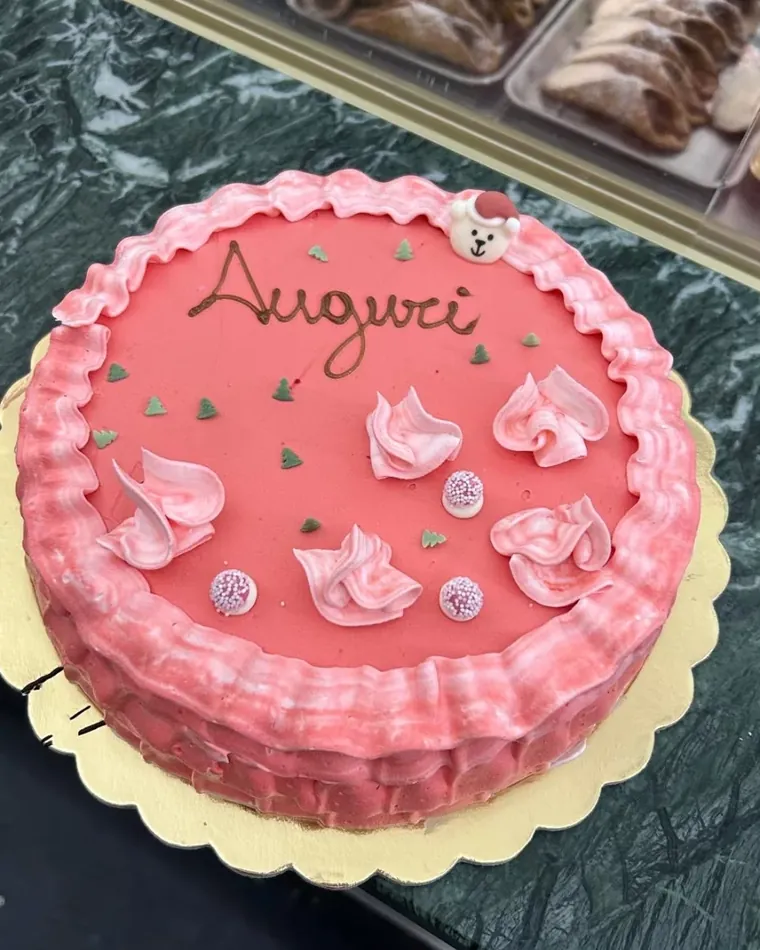 Torta rosa con scritta Auguri e decorazioni di panna